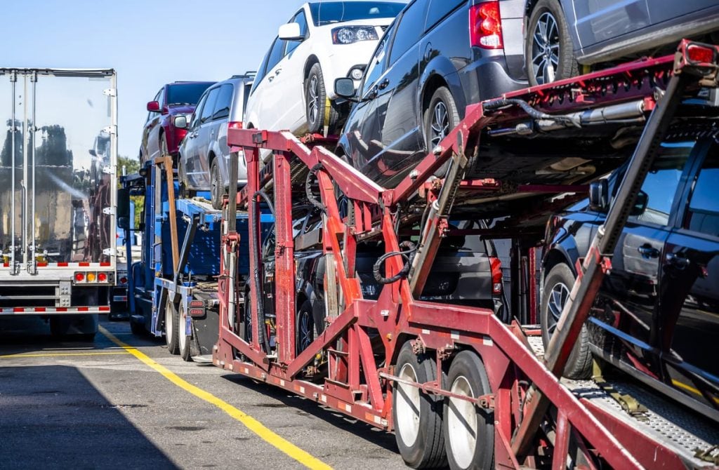 Big rig car hauler semi truck with loaded cars on semi trailer standing on truck stop parking lot beside another semi trucks
