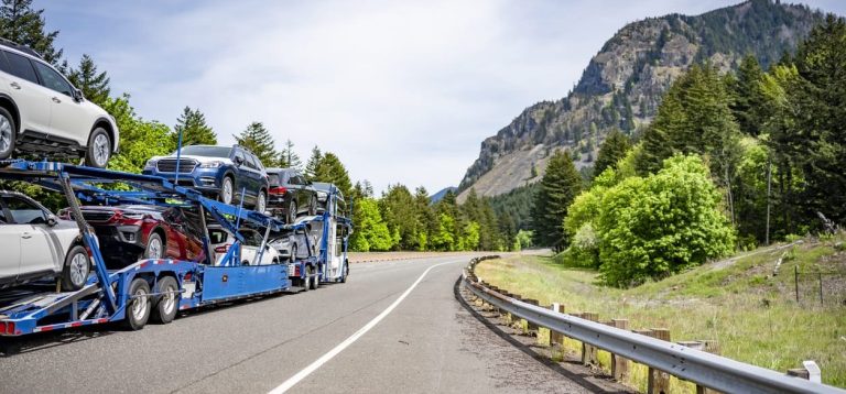 Loaded car carrier on a winding highway below a forested mountain