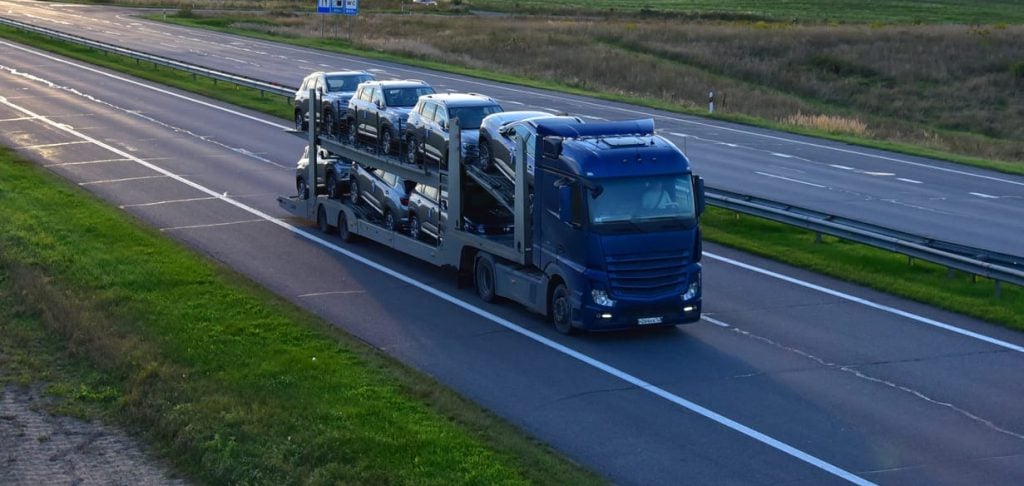 Car carrier trailer transports cars on highway. Auto transport and car shipping services concept.