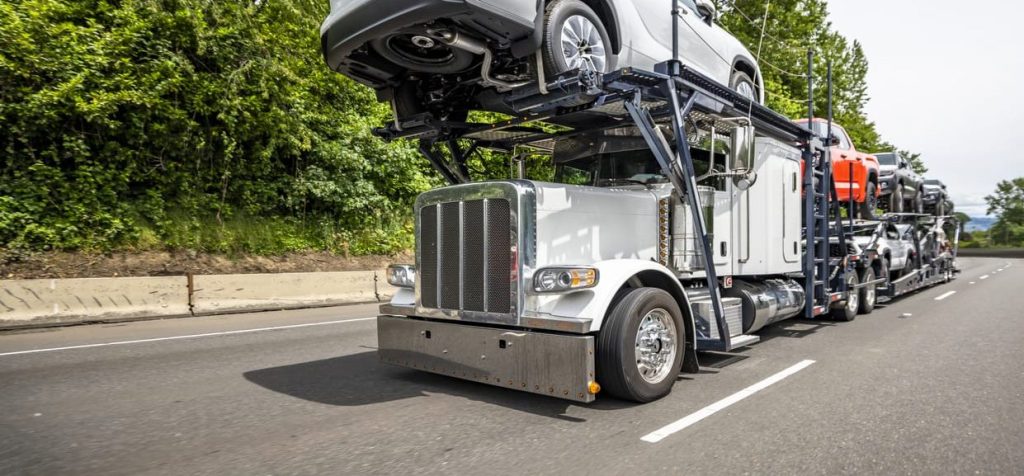 Professional industrial big rig car hauler semi truck transporting cars on two level modular semi trailer driving on the highway road