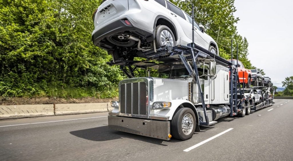 Professional industrial big rig car hauler semi truck transporting cars on two level modular semi trailer driving on the highway road