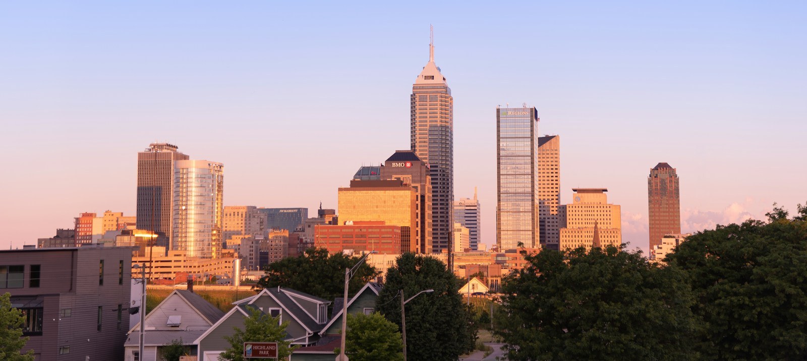 Downtown Indianapolis skyline at sunset with Salesforce Tower rising above the neighborhood rooftops