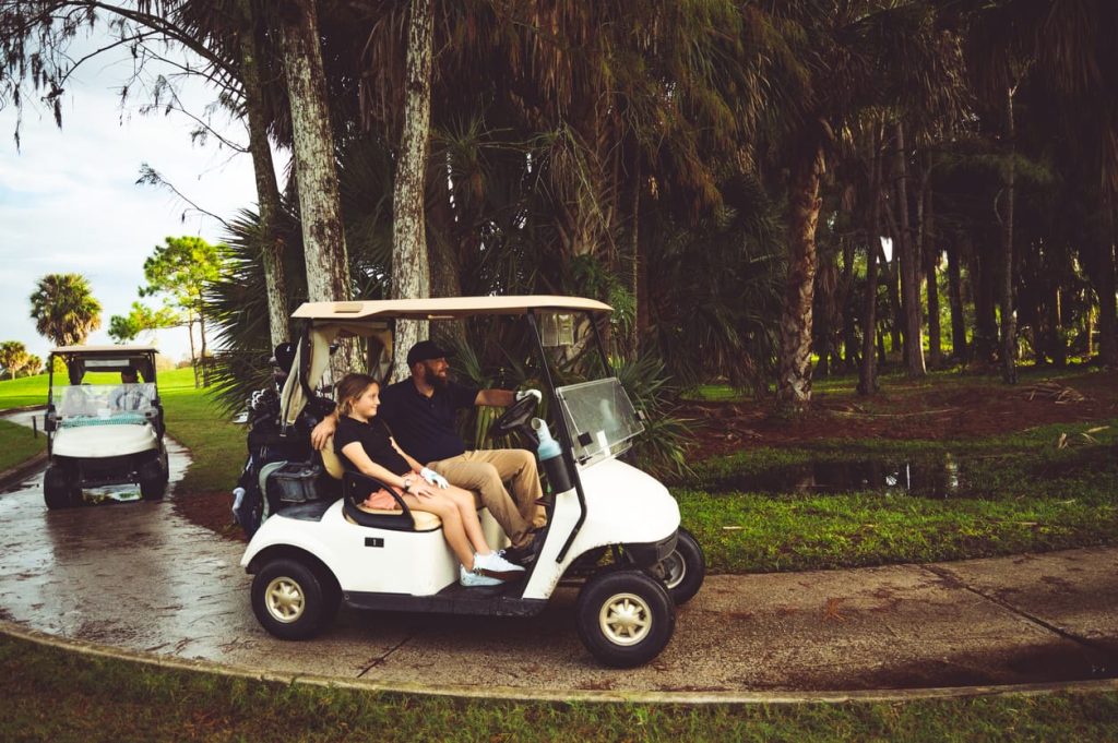 Fathers and their daughters ride in golf carts while playing a round of golf on a family outing
