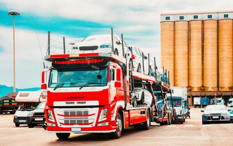 Car transporter on road at port of Cagliari in Sardinia Island, Italy summer. Truck trailer driving on motorway at highway. Mixed media.