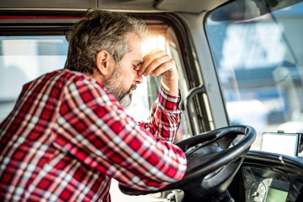 Tired mature truck driver waiting in traffic and contemplating about job problems.