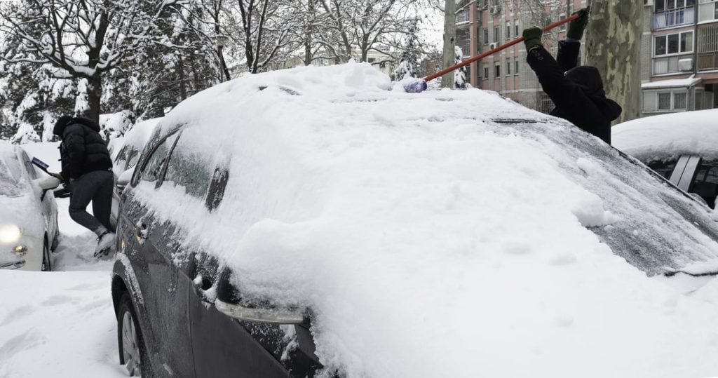 clearing snow-covered car into snowstorm