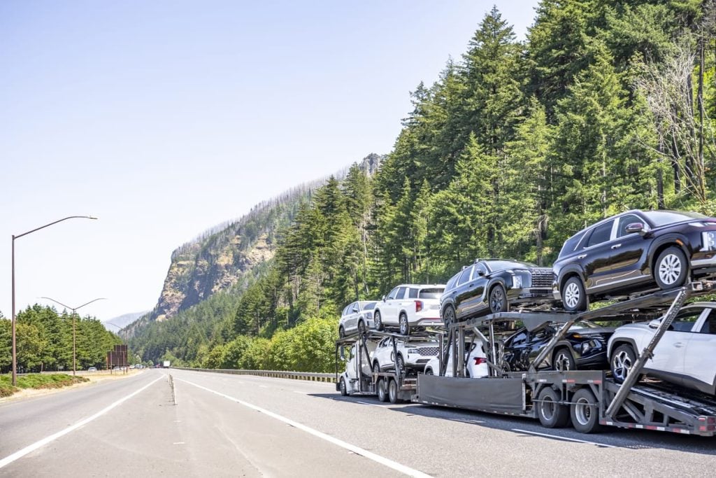 Car hauler white big rig semi truck transporting crossovers on the two hydraulic semi trailers driving on the one way highway road