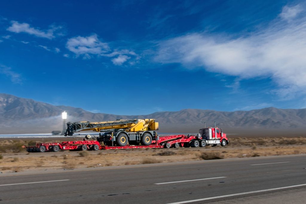 Red conventional tractor with a multi axle lowboy on a desert highway