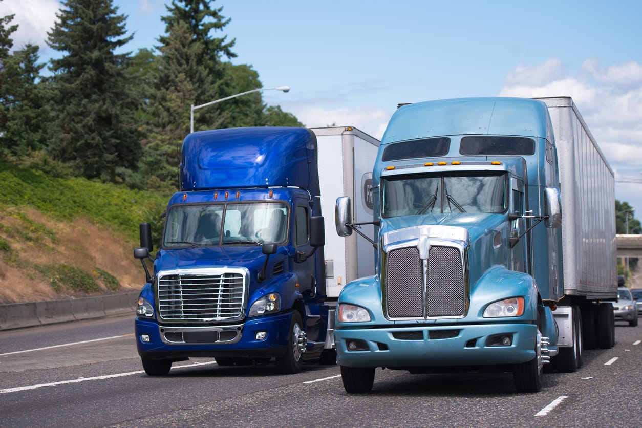 Two big rigs semi trucks in blue tone and different models with trailerd driving side by side