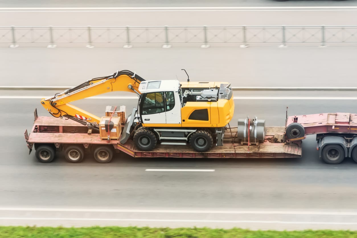 Trailer truck with long platform transport the Excavator on highway. Logistics of transportation of heavy and oversized cargo by road