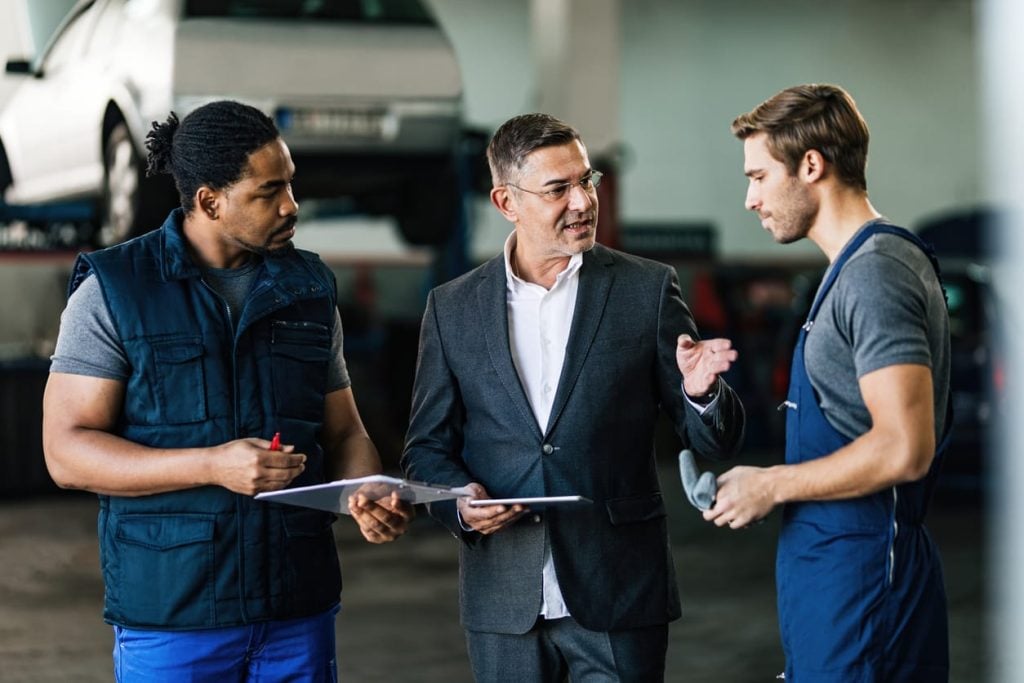 Three people talking beside cars in a dealership