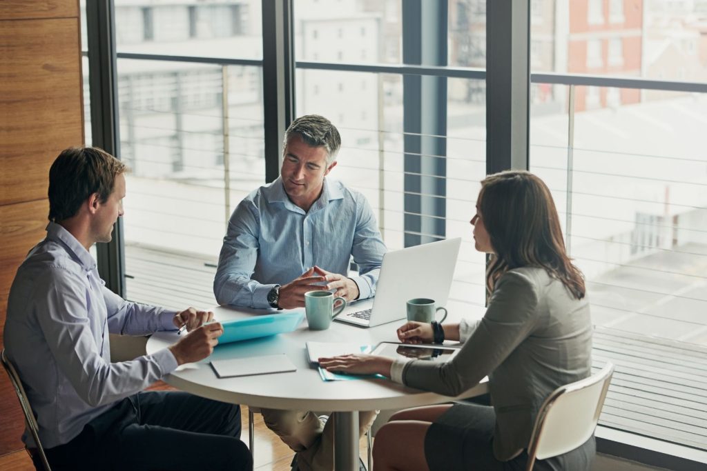 Three people talking around a table by a window