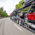 Classic big rig car hauler semi truck transporting cars on two level modular semi trailer running on the winding highway road