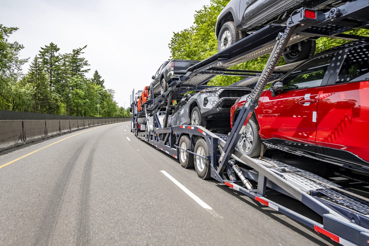 Classic big rig car hauler semi truck transporting cars on two level modular semi trailer running on the winding highway road