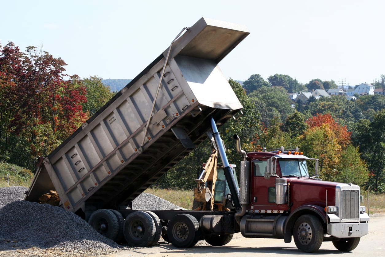 Tractor with an end dump trailer raising its bed to unload gravel