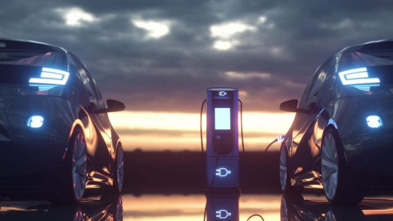 Two electric vehicles charging at a station at sunset