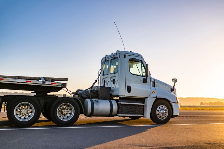 Day cab semi truck with an empty step deck trailer at sunset