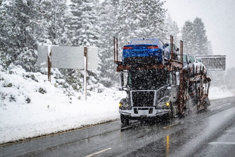 Car carrier hauling cars through falling snow on a mountain interstate