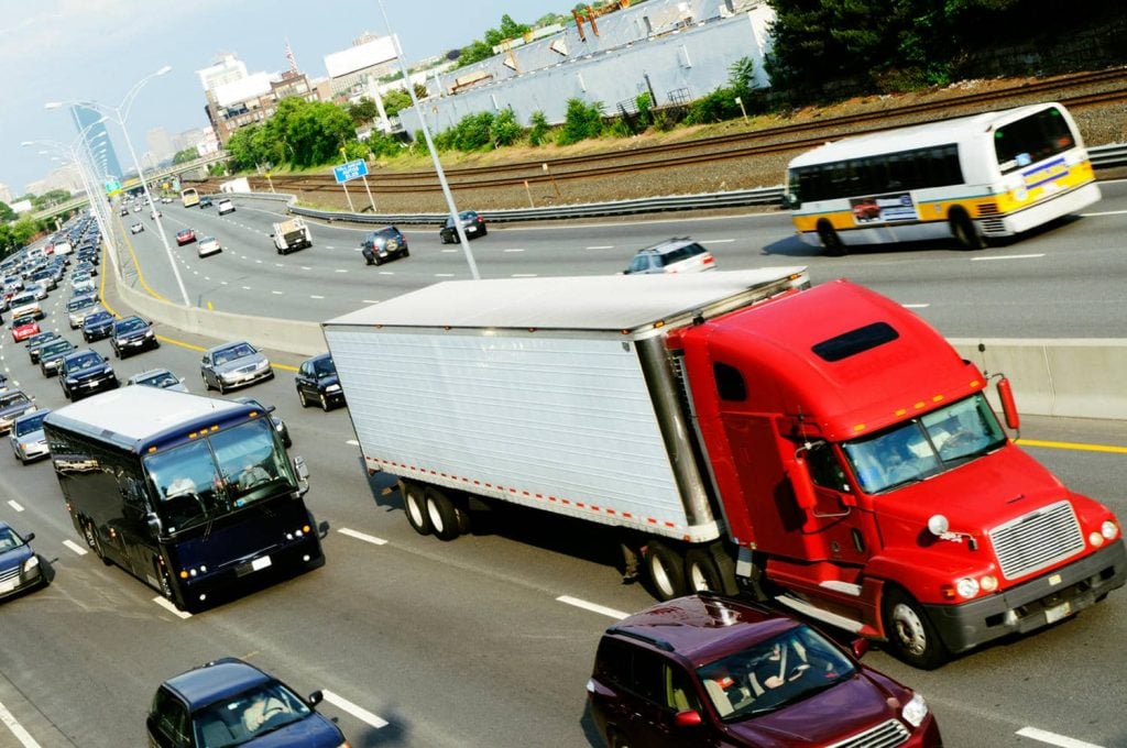 Red conventional tractor unit traveling an interstate highway