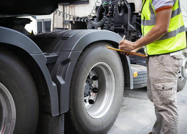 Inspector in a high visibility vest checking a truck tire with a clipboard