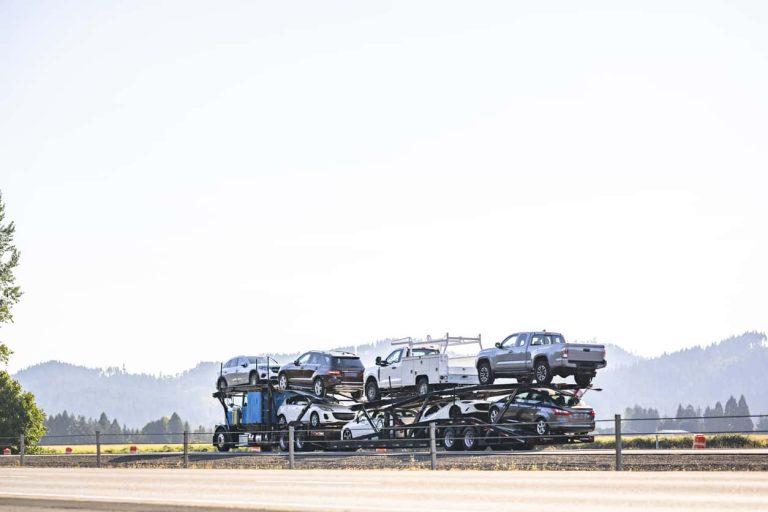 Blue classic old style big rig car hauler semi truck tractor transporting cars and crossovers on hydraulic semi trailer driving on the divided highway road in California