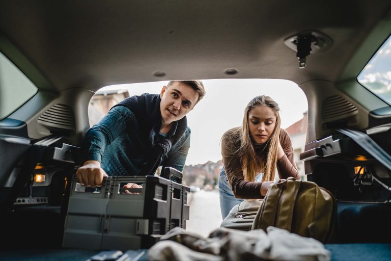 Two people couple students travel concept man and woman taking luggage baggage suitcase and other stuff and belongings from the back of car while moving into dormitory on college campus real people