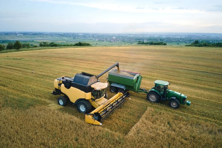 Aerial view of combine harvester unloading grain in cargo trailer working during harvesting season on large ripe wheat field. Agriculture and transportation of raw farm products concept