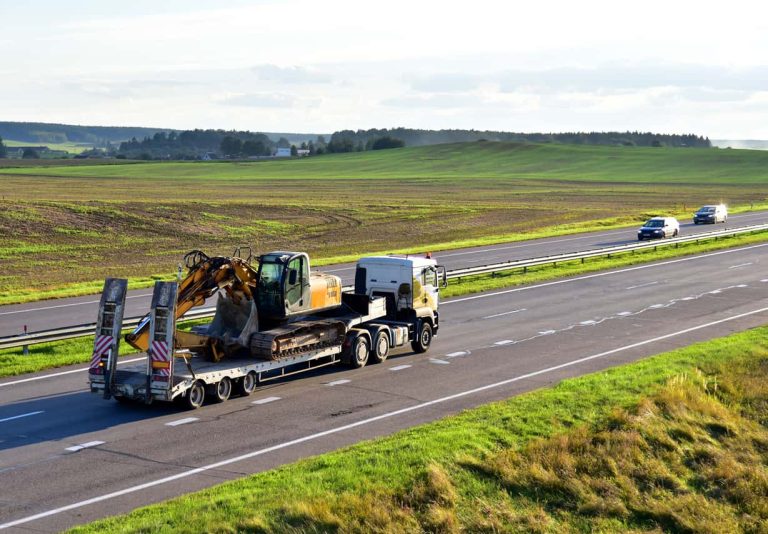 Trailer truck with long platform transport the Excavator on highway. Earth mover backhoe on heavy duty flatbed vehicle for transported.