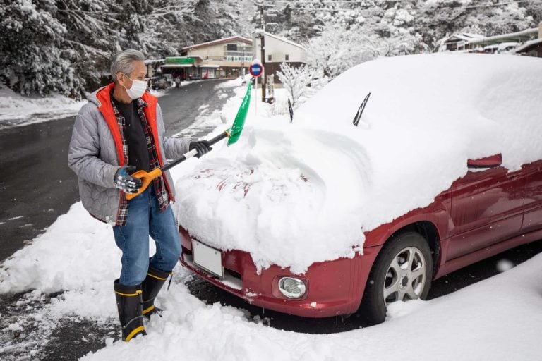 A senior shoveling snow off his car in winter