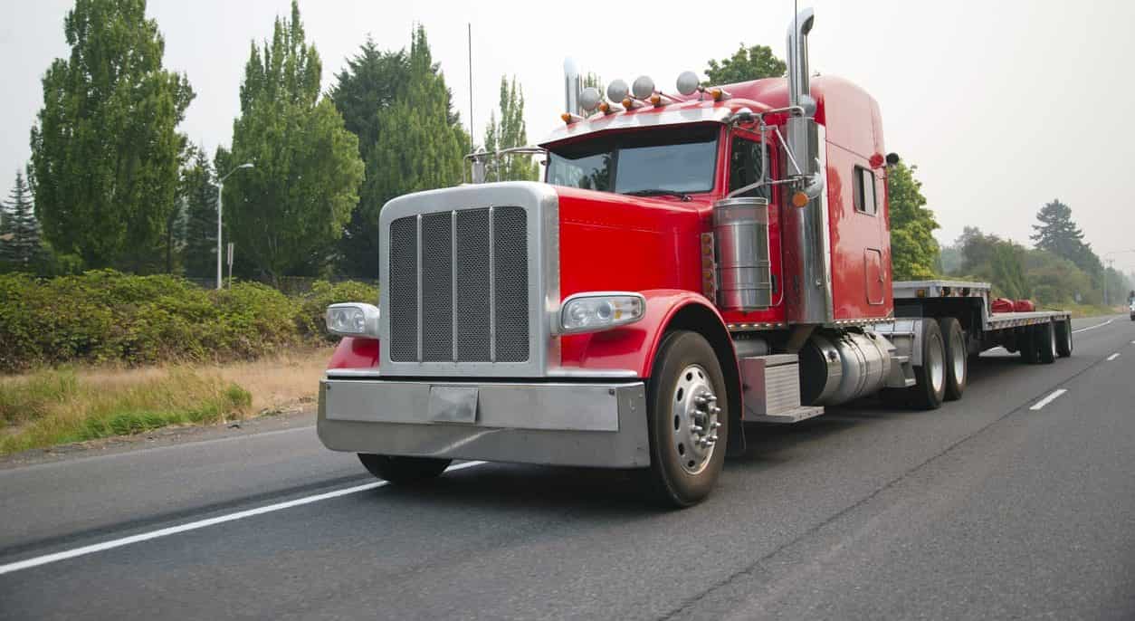 Powerful red big rig semi truck with flat bed step down semi trailer move on road for loading cargo