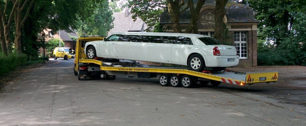 A white stretch limousine loaded on a yellow flatbed transport trailer
