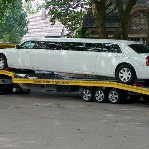 A white stretch limousine loaded on a yellow flatbed transport trailer