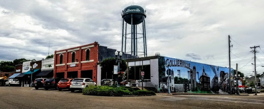 The Collierville water tower rising over Main Street storefronts and the town mural in Collierville, Tennessee
