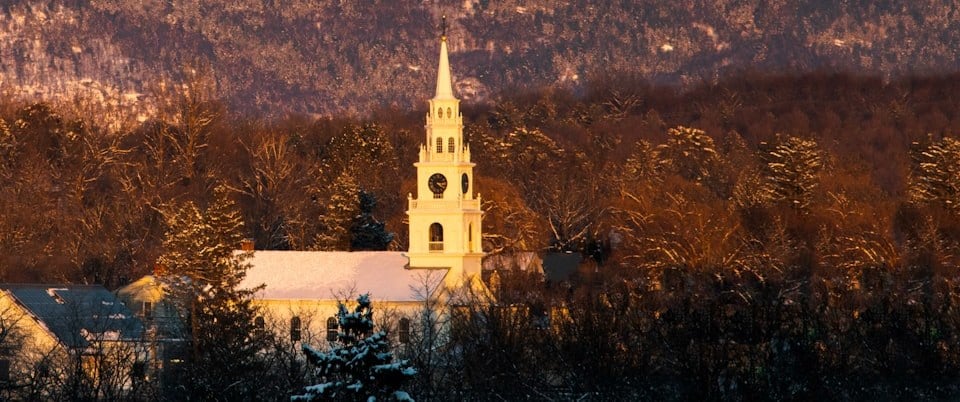 The white steeple of the Middlebury Congregational Church glowing at dusk beneath the Green Mountains in Middlebury, Vermont