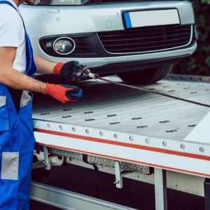 Driver strapping a car to a flatbed carrier