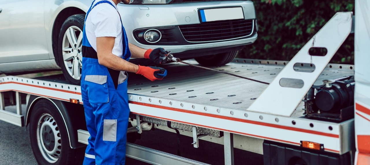 Driver strapping a car to a flatbed carrier