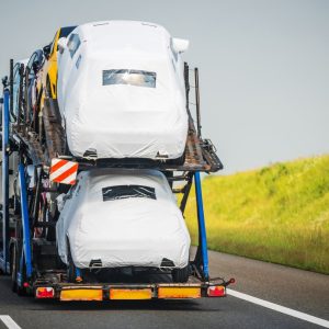 Car carrier trailer loaded with protected new vehicles driving down the highway