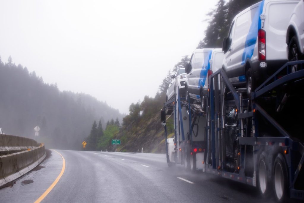 Car hauler semi truck carrying white vans on a rainy mountain highway