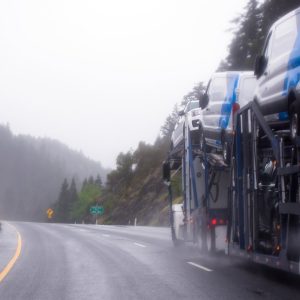 Car hauler semi truck carrying white vans on a rainy mountain highway