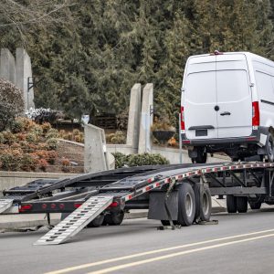 White cargo van on a car hauler trailer with loading ramps down on a residential street