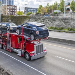 Red car hauler semi truck transporting SUVs on an urban highway
