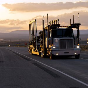 Car hauler semi truck driving on an open highway at sunset