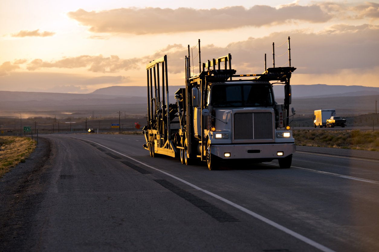 Car hauler semi truck driving on an open highway at sunset
