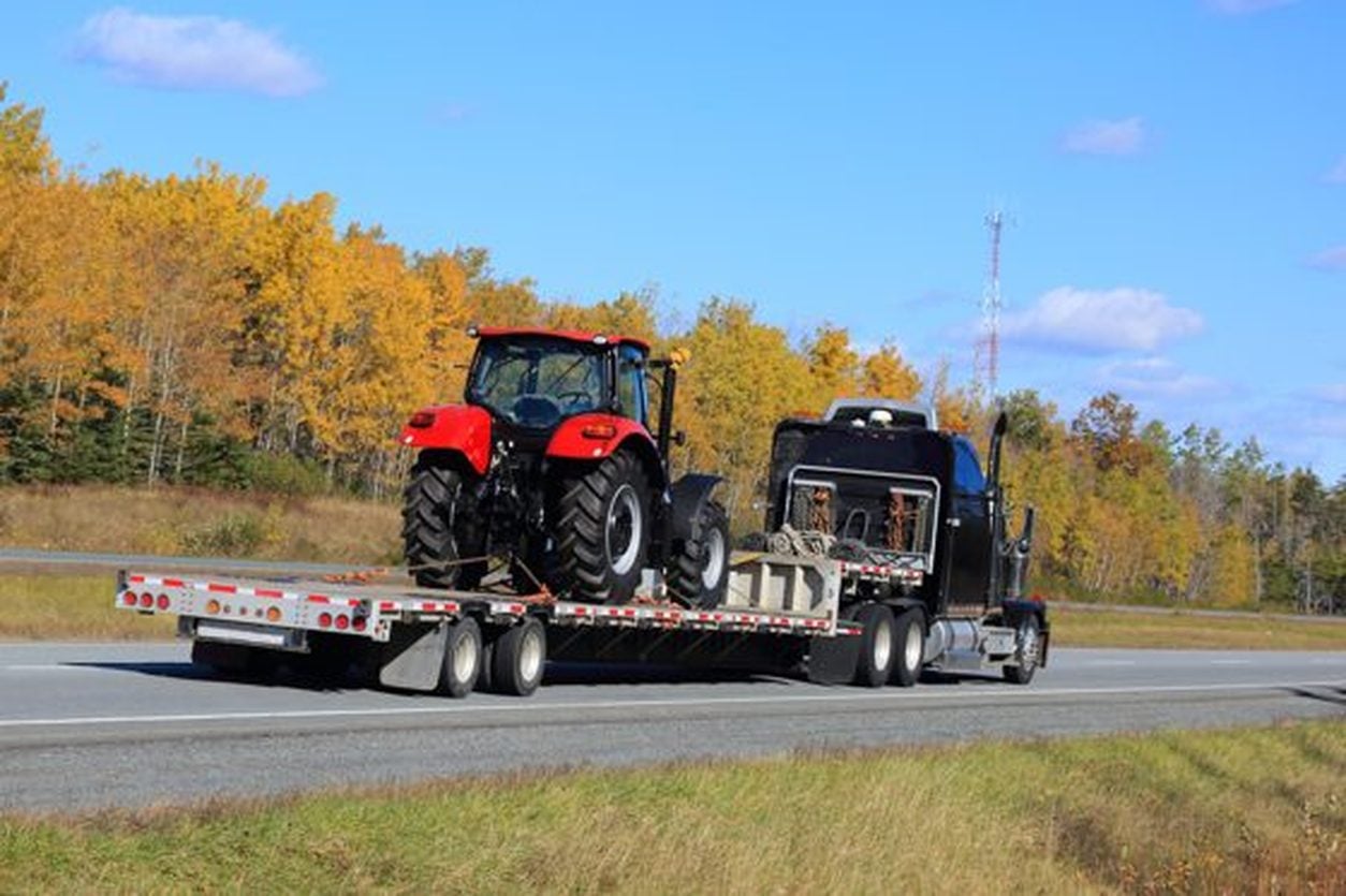New red tractor secured on a step deck trailer behind a semi truck