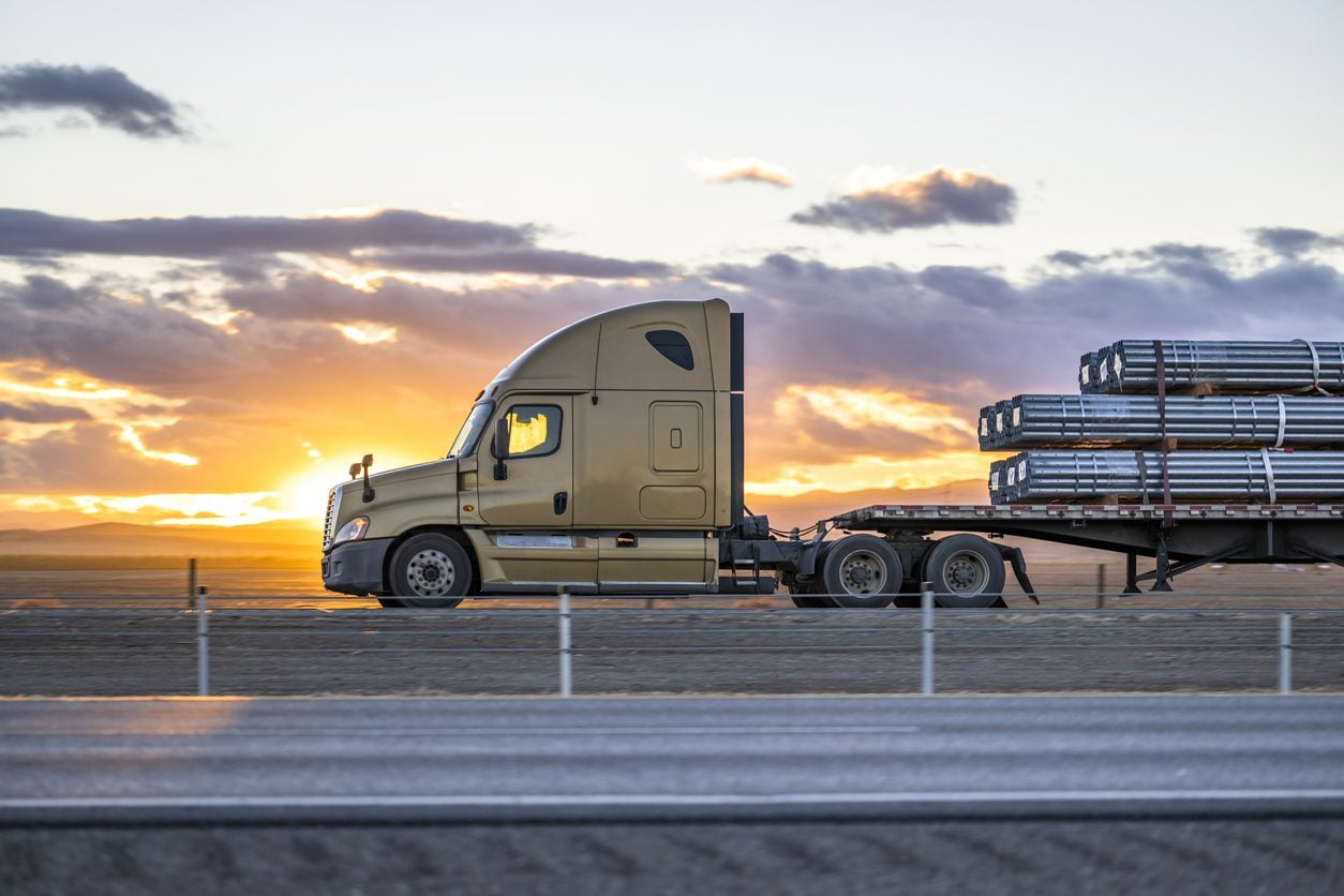 Conventional tractor with a loaded flatbed trailer at sunset