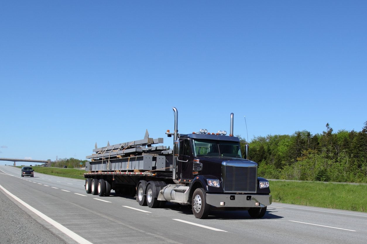 Black conventional tractor hauling a load on a flatbed trailer