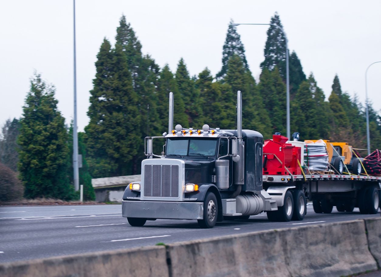 Black conventional tractor with a secured flatbed load