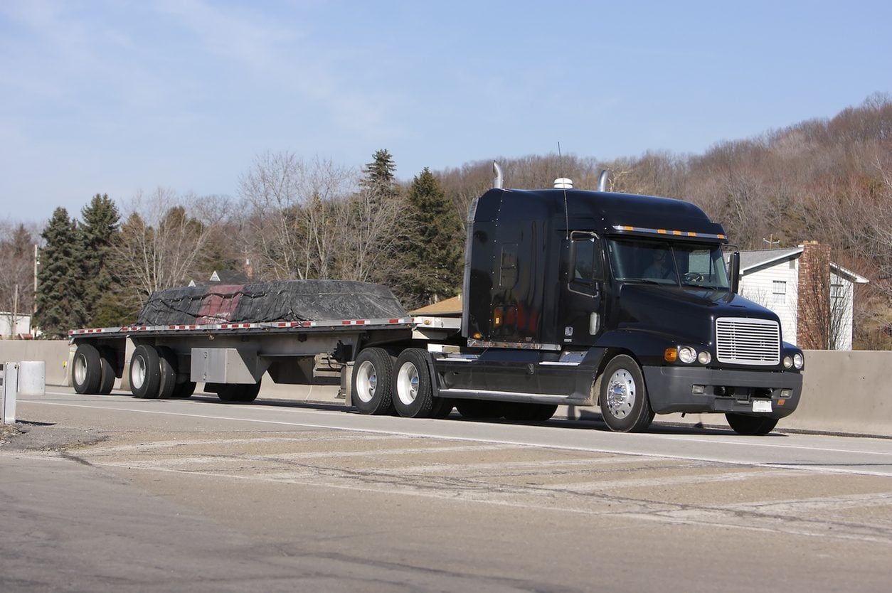 Black conventional tractor with a loaded flatbed trailer