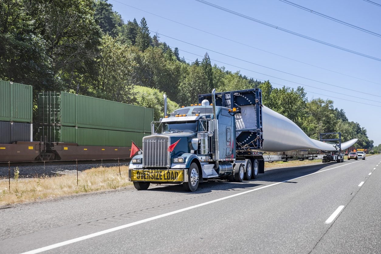 Oversize load banner on a truck hauling a turbine blade with escort vehicles behind