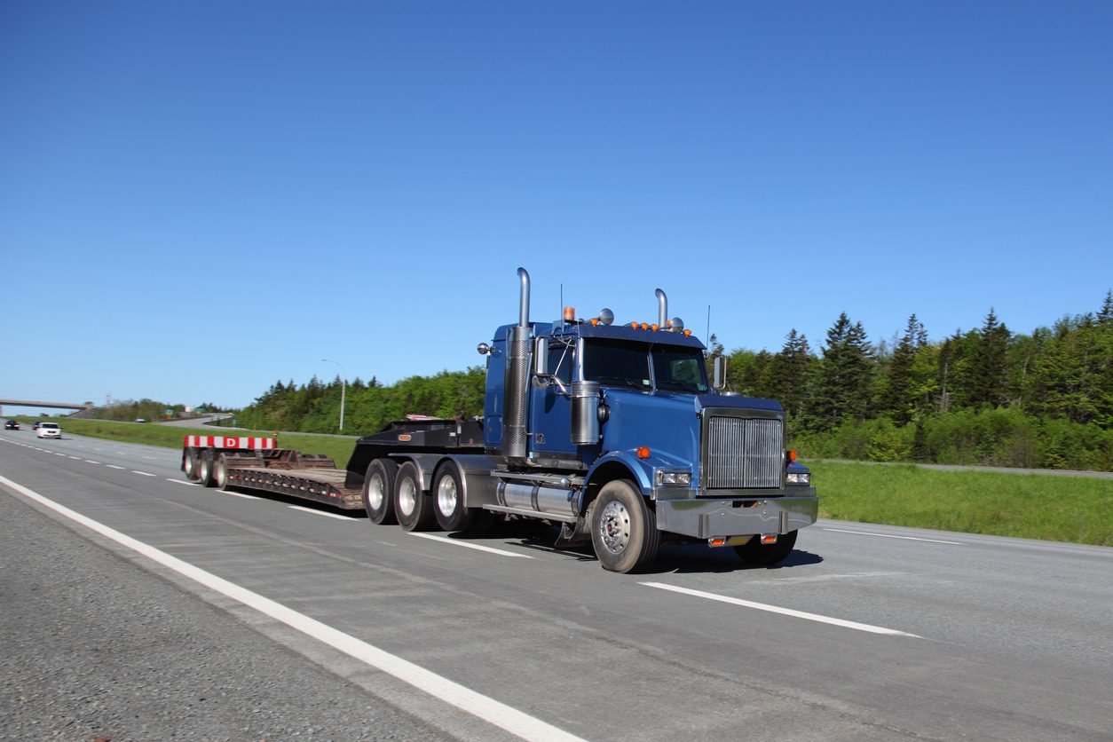 Blue conventional tractor with an empty lowboy trailer on a highway